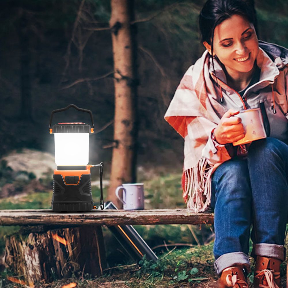 Camper with a mug beside the lit lantern at dusk